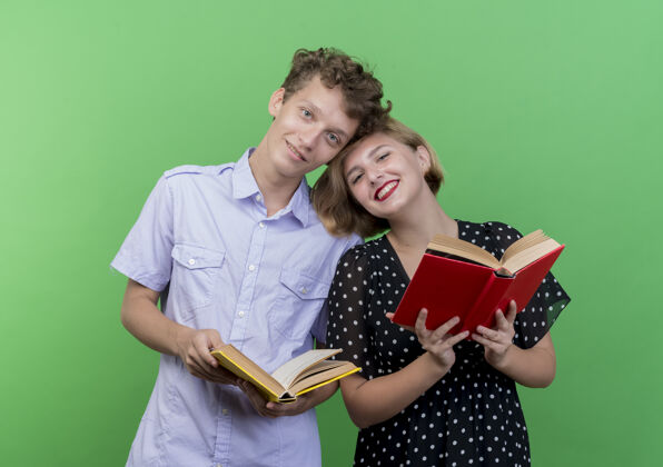 站着年轻漂亮的夫妇站在一起拿着书幸福而积极的微笑站在绿色的墙上微笑年轻抱着
