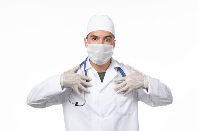 冠状病毒正面图：男医生穿着医疗服 戴着口罩 因白墙病毒性冠状病毒病男性制服套装
