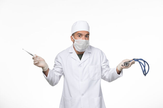 大流行正面图身穿防毒服和口罩的男医生手持听诊器对着白色桌面病毒冠状病毒-疾病大流行实验室外套医疗视图