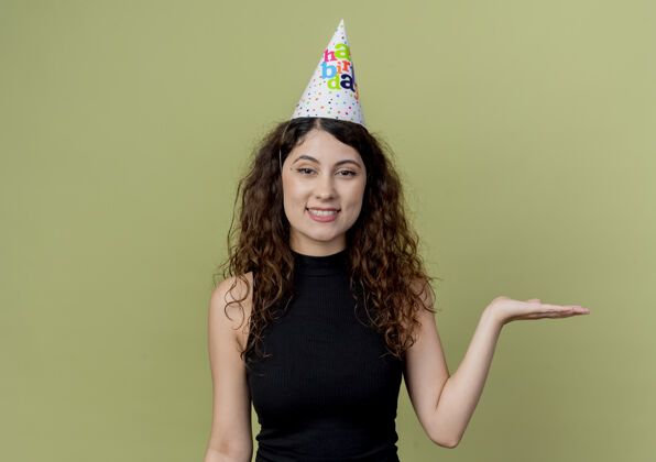 站立一位年轻漂亮的女士 卷发 戴着节日帽 手挽着手 微笑着 站在橙色的墙上 展示生日派对的概念手年轻展示
