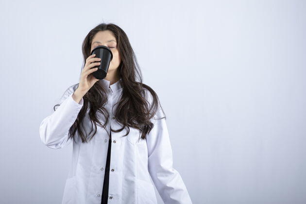 医药女医生在灰色的画像上喝着一杯咖啡女性治疗师外套