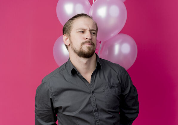 站年轻人举着一堆气球 站在粉红色的墙上困惑地看着一边庆祝生日看男人气球