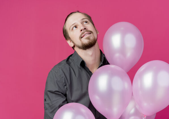 束年轻人举着一堆气球庆祝生日站在粉红色的墙上沉思着举行气球看