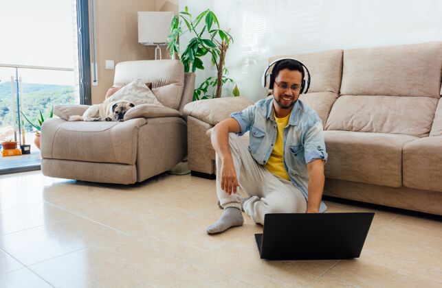 帅气一个男人坐在地板上听音乐 在家里用笔记本电脑工作的水平镜头男人人笔记本电脑