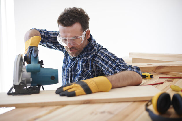 男建筑工人用电锯办公桌设备木板