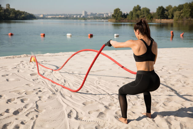 阳刚年轻健康的女人在沙滩上用绳子锻炼身体空气手臂运动