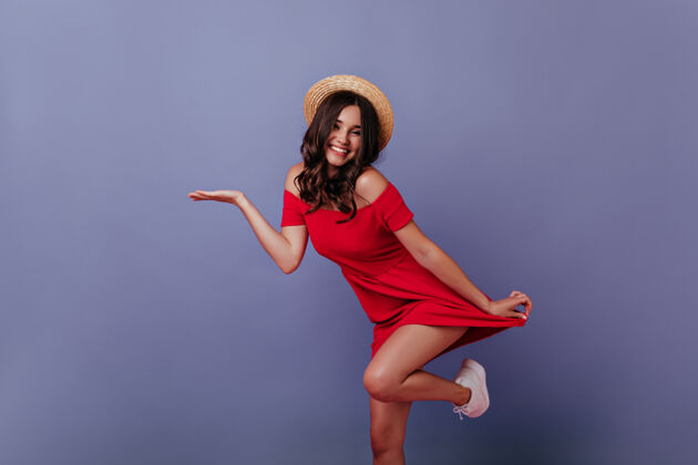 肖像一个戴草帽的白人女孩在紫色的墙上摆姿势一个穿着红裙子的迷人女人在跳舞现代成人服饰