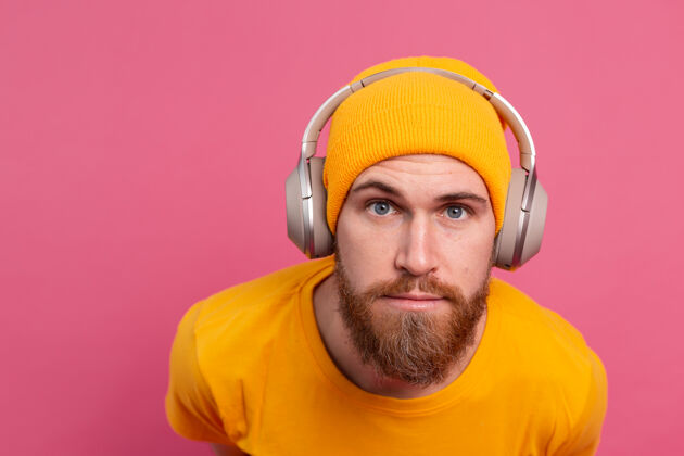 音频帅哥在随意地听着音乐 用耳机隔离在粉色背景上粉色放松快乐