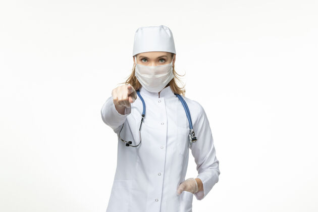 套装正面图女医生穿着医疗服戴着口罩和手套因冠状病毒在浅白的办公桌上大流行冠状病毒病到期听诊器手套