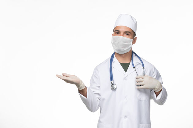 疾病正面图：男医生穿着医疗服 戴着口罩 在白色桌面上用听诊器抵御冠状病毒-病毒疾病大流行办公桌男性医疗