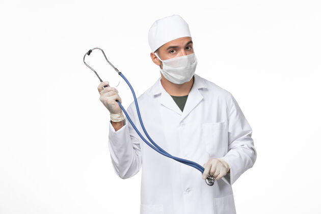 实验室外套正面图男医生身穿医疗服 戴口罩 因白墙上戴着柯维听诊器 柯维病毒大流行听诊器视图男性
