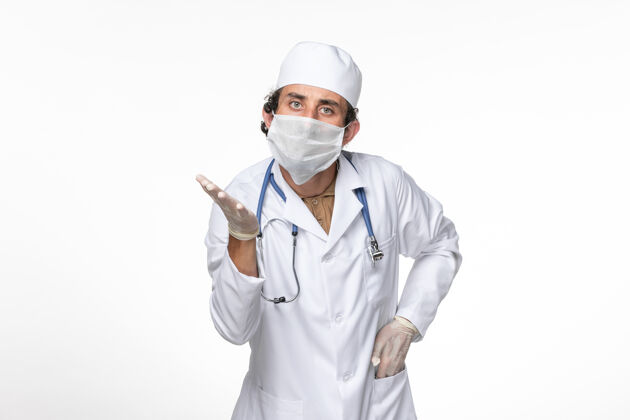 桌子正面图：男医生穿着医疗服 戴着无菌口罩 以防白色办公桌上的冠状病毒飞溅病毒大流行大流行医疗套装