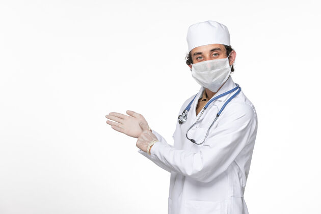正面正面图：男医生穿着医疗服 戴着口罩 以防冠状病毒在白墙上传播医疗面罩医生