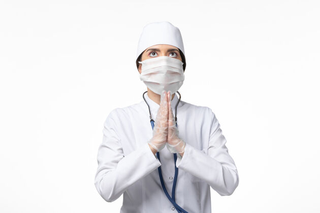 疾病正面图：女医生穿着白色无菌医疗服 带着口罩 因为柯维德-祈祷白墙疾病柯维德-大流行病毒疾病专业面具人