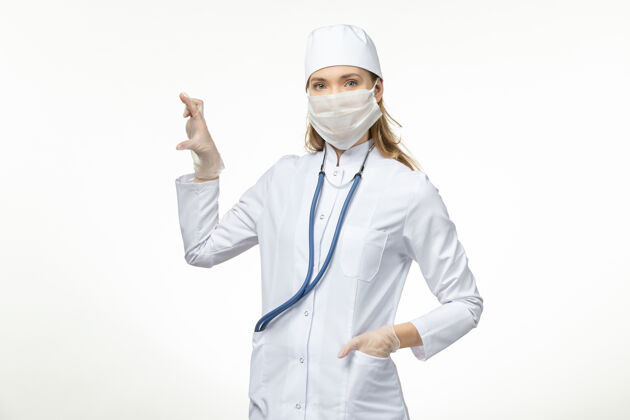 听诊器前视图：穿着白色医疗服 戴着口罩的女医生在白墙上抵御冠状病毒的传染大流行正面女性