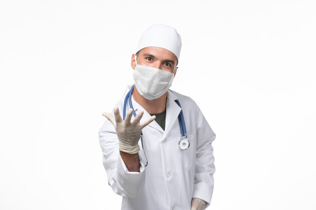 听诊器正面图：男医生穿着医疗服 戴着口罩 因为白墙上有冠状病毒大流行疾病药品正面套装
