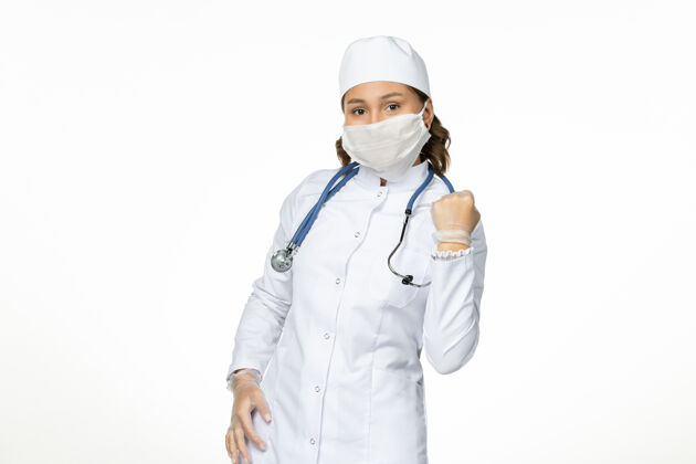 女性正面图女医生身穿白色医疗服 戴着口罩因冠状病毒欣喜于白墙大流行性疾病隔离冠状病毒正面套装冠状病毒
