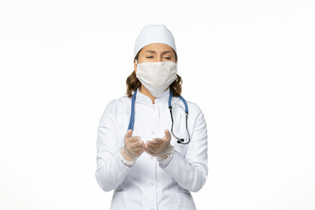 冠状病毒前视图女医生穿着白色医疗服 戴着口罩 由于白色地板上有冠状病毒病大流行病毒大流行人员疾病