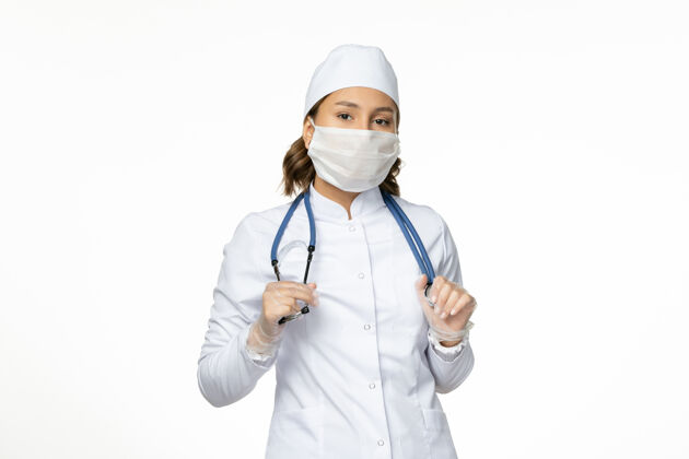 疾病正面图：穿着白色医疗服 戴着白色面罩的女医生在淡白色的墙壁上吃潘多米病毒病药疾病女性医院