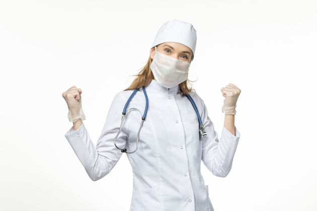 视图正面图女医生穿着医疗服戴着口罩和手套因冠状病毒在白色办公桌上大流行冠状病毒疾病成人制服