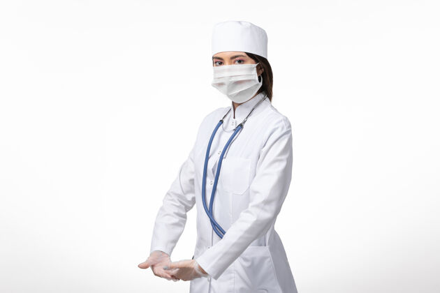 冠状病毒前视图女医生穿着白色医疗服 戴着口罩 由于白色墙上有冠状病毒 医学病毒大流行 可维氏病毒女性专业套装