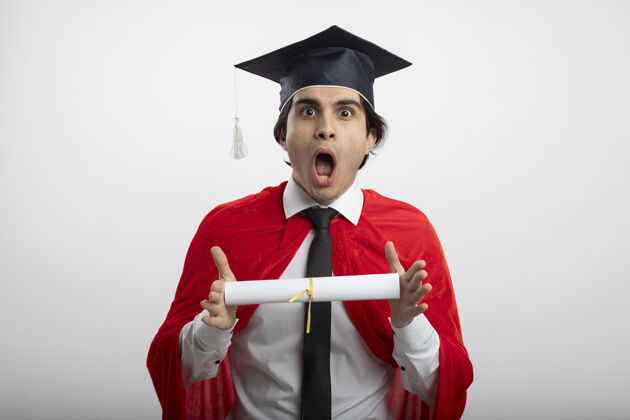 戴着一个年轻的超级英雄戴着毕业帽 打着领带 拿着毕业证书 看着摄像机 吓坏了帽子看着小伙子