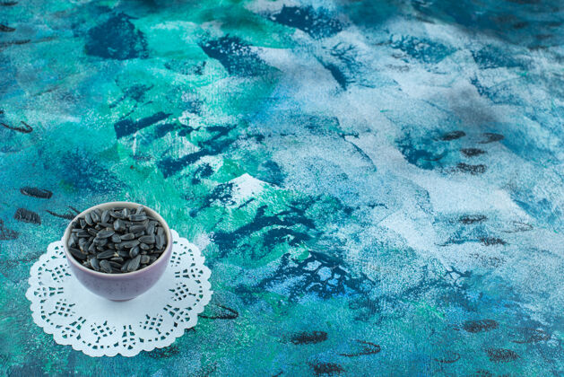 碗未去皮的葵花籽放在碗里 在蓝色的杯垫上美味美味果仁