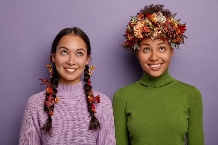 紫色秋天的概念快乐的年轻多种族女性穿着休闲服 注意力集中在上面 有着牙齿般的微笑 头发上戴着秋叶和浆果 欢庆秋天的折扣 在室内摆姿势女孩女人多样性