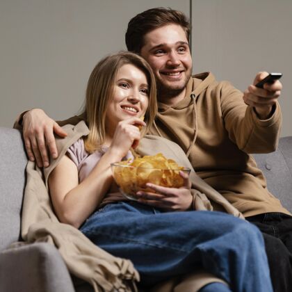 沙发夫妻俩在沙发上看电视吃薯片女人室内看电视