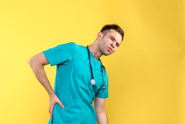 医院黄墙上背疼的年轻男医生的正面图冠状病毒成人肖像