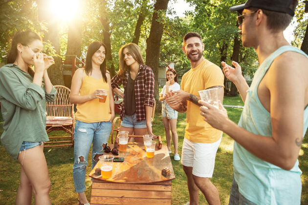 烧烤一群快乐的朋友在阳光明媚的日子里喝着啤酒 一起烧烤一起在户外的林间空地或后院休息友谊酒精烹饪