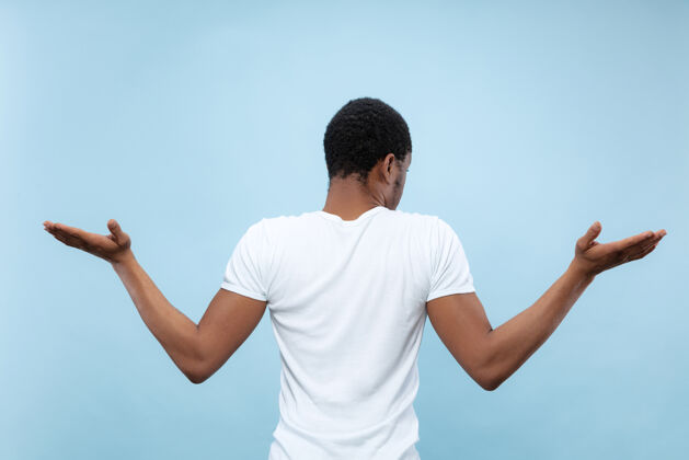 男人蓝色空间上穿着白衬衫的非洲裔年轻人的半身特写肖像人类情感 面部表情 广告 销售理念不确定性 怀疑广告手势工作