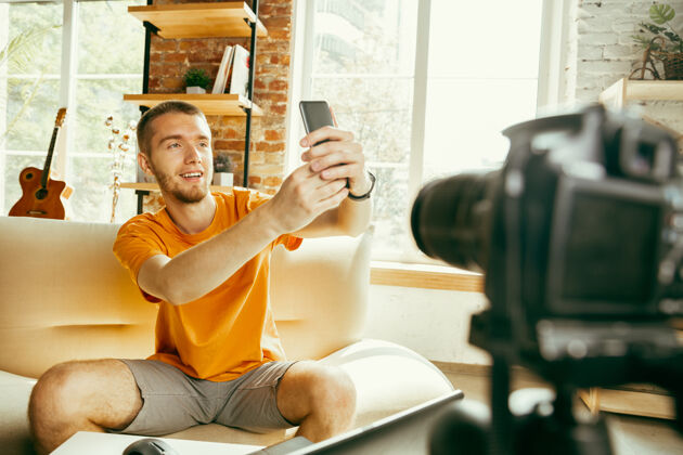 通信年轻的白人男性博主用专业相机录制视频评论智能手机在家在线视频博客男性