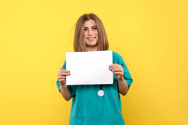 年轻女医生黄色墙上拿着文件的年轻女医生的正视图漂亮前面微笑