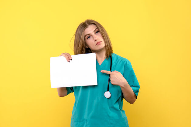 医学黄色墙上拿着文件的年轻女医生的正视图医院年轻女医生持有