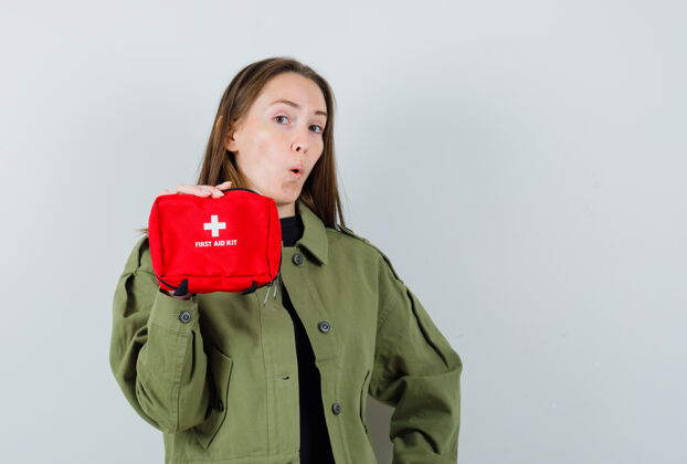 微笑身穿绿色夹克的年轻女子展示急救箱 正视图工具包时尚援助
