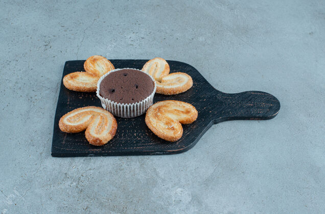 口感薄片饼干和一个在大理石背景的黑色板上的纸杯蛋糕高质量的照片纸杯蛋糕烘焙甜点
