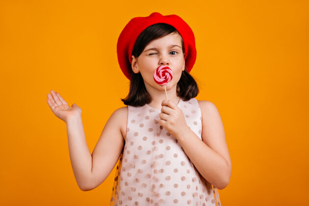 黑发快乐的孩子吃棒棒糖一头短发的未成年少女 黄色上有糖果女孩表情吃