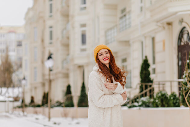 外套迷人的长发女孩在模糊的街道上摆姿势姜黄色头发的迷人女模特享受冬天黑发街头风格帽子