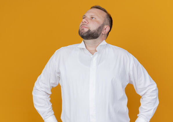 穿一个留着胡子的男人穿着白衬衫 表情严肃地站在橘色的墙上 一边看一边严肃男人表情