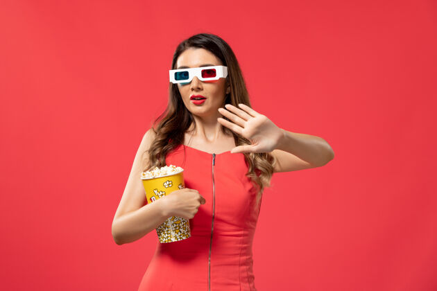 爆米花正面图年轻女性手持爆米花包戴着d墨镜在红色表面前面电影太阳镜