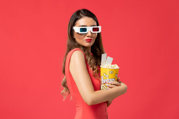 性感正面图红色表面上戴着d墨镜拿着爆米花的年轻女性前面电影院票