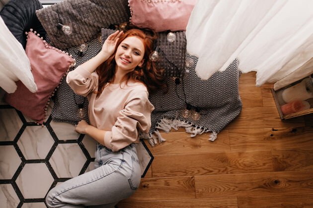 女人一个穿着牛仔裤的红发女孩坐在枕头旁 笑嘻嘻的姜女躺在地板上的室内照片快乐女孩年轻