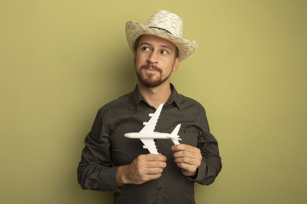 衬衫一个穿着灰色衬衫 戴着夏帽的年轻帅哥 手里拿着玩具飞机 脸上带着羞涩的微笑向一旁望去抱着旁边男人