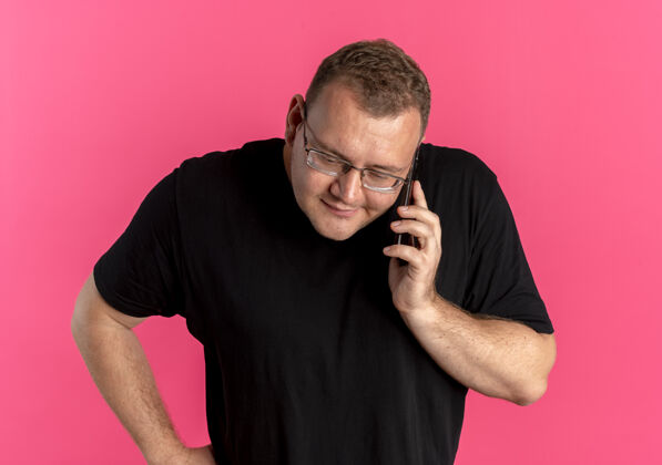 而一个戴眼镜 身穿黑色t恤的超重男子站在粉红色的墙上一边打手机一边争吵男人说话争辩