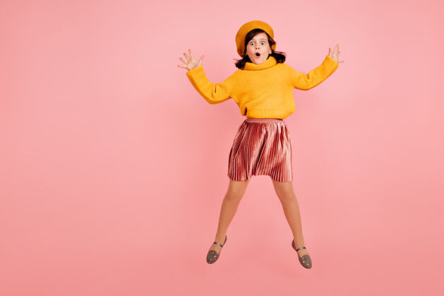 快乐穿着黄色毛衣的跳女孩兴奋的孩子在粉红色的墙上跳舞运动年轻休闲