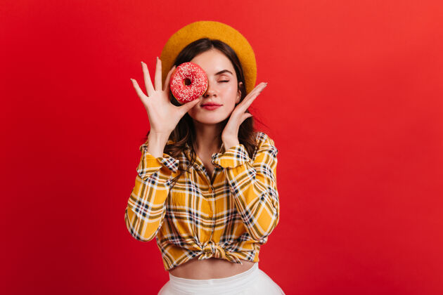 女性心情很好的年轻女孩用草莓甜甜圈遮住眼睛戴着贝雷帽的红唇女人闭着眼睛在隔离墙上摆姿势女人法国肖像