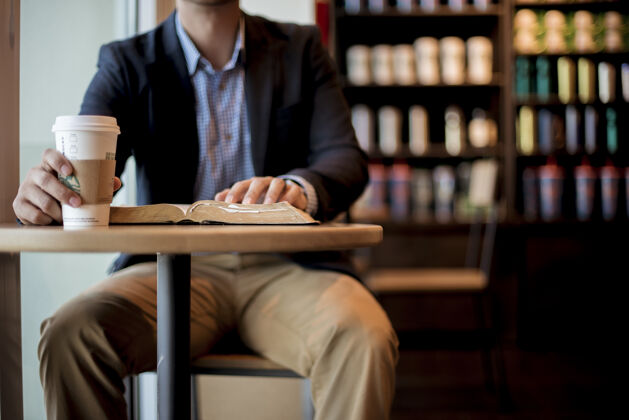 圣经一个穿着黑色外套拿着白色一次性杯子的男人书房酒吧阅读