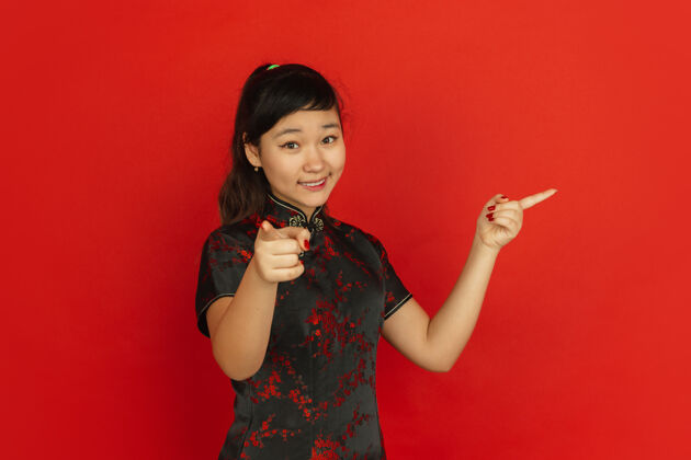 服装指指点点 面带微笑中国新年快乐红色背景上的亚洲少女肖像身着传统服装的女模特看起来很快乐庆祝 人类情感复制空间旗袍文字空间红色