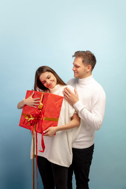 美丽美丽的情侣在蓝色的工作室墙上相爱礼物拥抱礼物